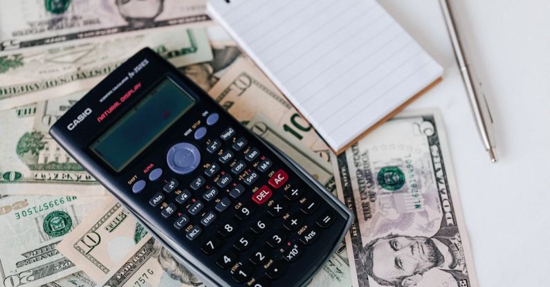 Wealth Strategy - From above electronic calculator and notepad placed over United States dollar bills together with metallic pen for budget planning and calculation