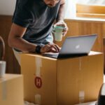 Real Estate Investment - Ethnic man typing on laptop while preparing to relocate