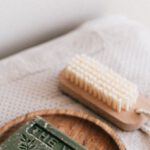 Sustainable Investing - From above composition with natural green soap on eco friendly wooden holder and sustainable brush lying on folded clean soft fresh gray towels against white wall