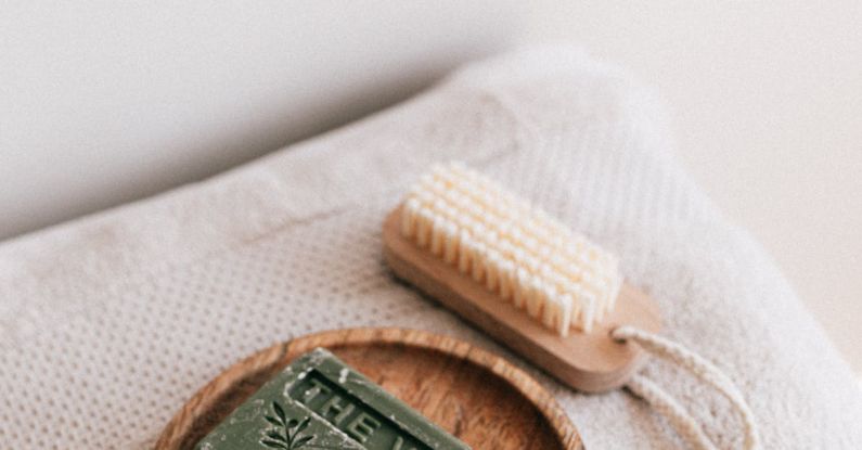 Sustainable Investing - From above composition with natural green soap on eco friendly wooden holder and sustainable brush lying on folded clean soft fresh gray towels against white wall