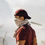 Sustainable Agriculture - Unrecognizable man with scarf on face walking in sandy terrain terrain near windmills