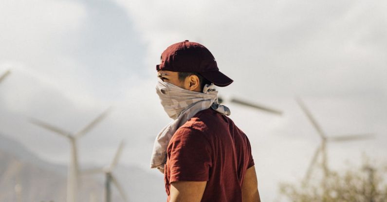 Sustainable Agriculture - Unrecognizable man with scarf on face walking in sandy terrain terrain near windmills