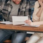 Couple Finance - A Couple Sitting Near the Wooden Table while Looking at the Document in Shocked Emotion