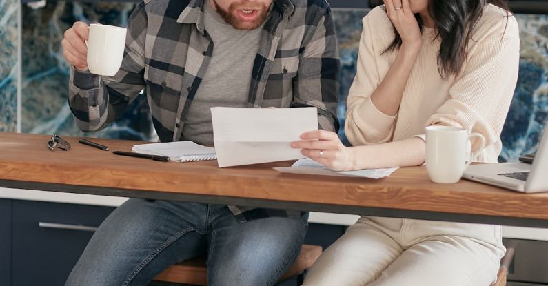 Couple Finance - A Couple Sitting Near the Wooden Table while Looking at the Document in Shocked Emotion