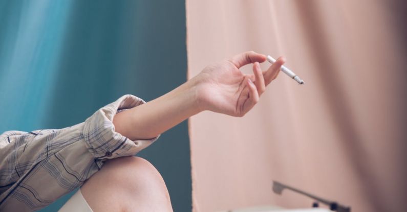 Risk Tool - Unrecognizable female sitting at white table with typewriter near blue and pink curtain while holding cigarette in hand