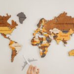 Geographic Diversification - Crop unrecognizable person with toy aircraft near multicolored decorative world map with continents attached on white background in light studio