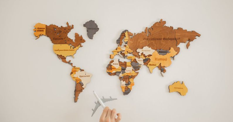 Geographic Diversification - Crop unrecognizable person with toy aircraft near multicolored decorative world map with continents attached on white background in light studio