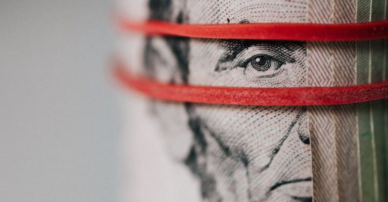 Trade Tensions - Closeup of rolled United States five dollar bills tightened with red rubber band
